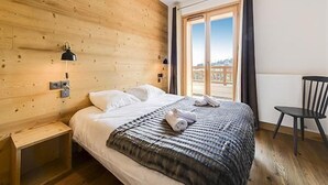A bedroom with a wooden wall, a bed with white linens, a black chair, and a window with a view. - Wifi, view mountain, swimming pool, sauna, hammam, balcony, tv, ski locker, 80-95m², Combloux (Combloux)