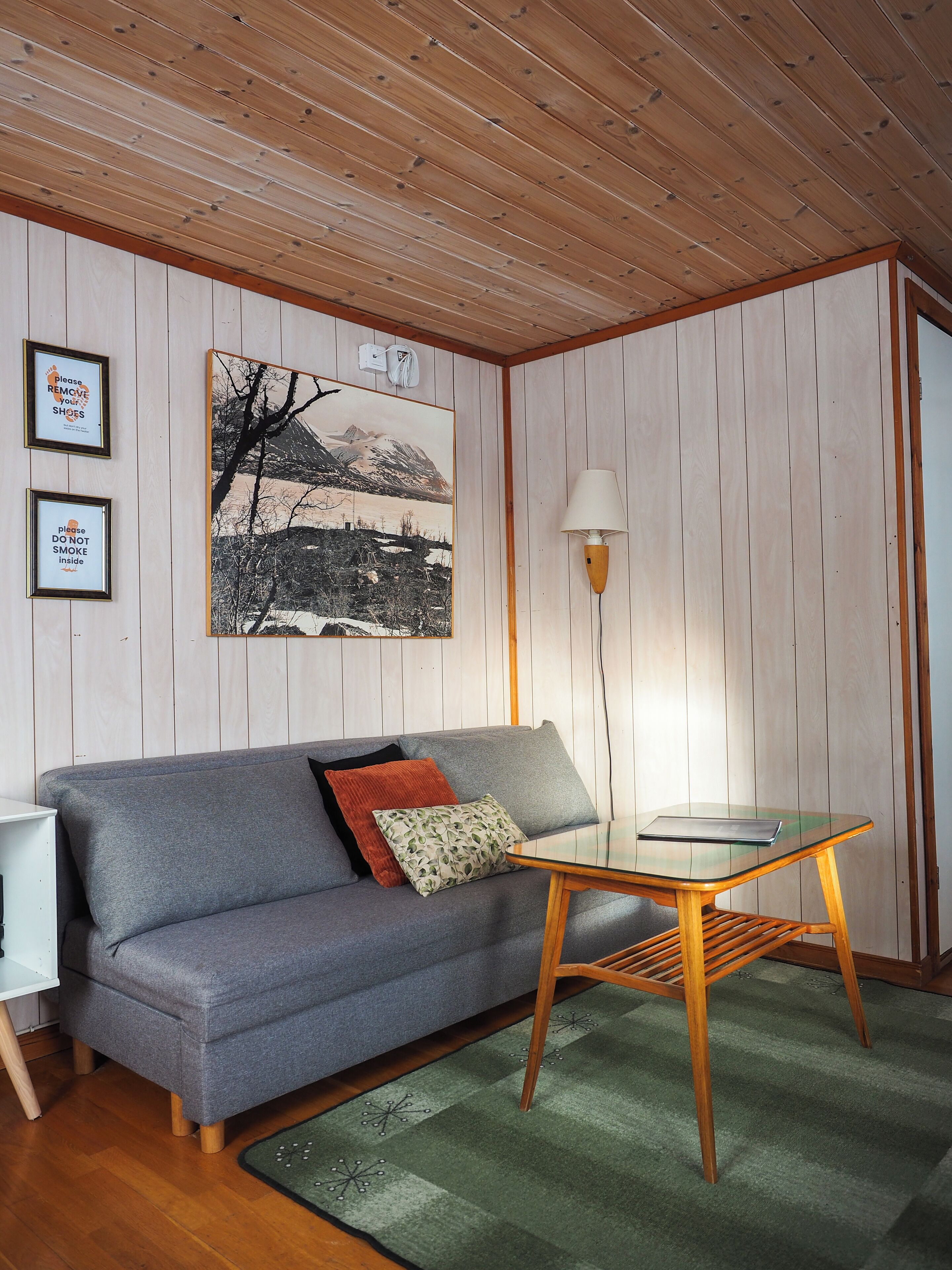 Una habitación con sofá gris, una mesita de vidrio, una lámpara y un cuadro en la pared.