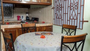Un comedor con una mesa redonda cubierta por un mantel blanco con diseños morados y anaranjados, rodeado de sillas de madera.