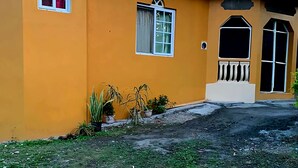 Un edificio con fachada amarilla, varias ventanas y un pequeño porche con plantas en macetas.