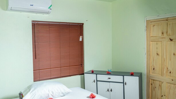 Un dormitorio con cama, cortinas blancas, un armario de madera y un equipo de aire acondicionado.