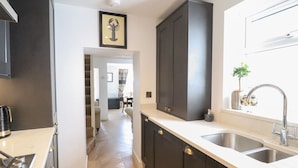 A modern kitchen with dark cabinets, a stainless steel sink, and a herringbone-patterned floor. - 3 Rosemary Lane (Conwy)