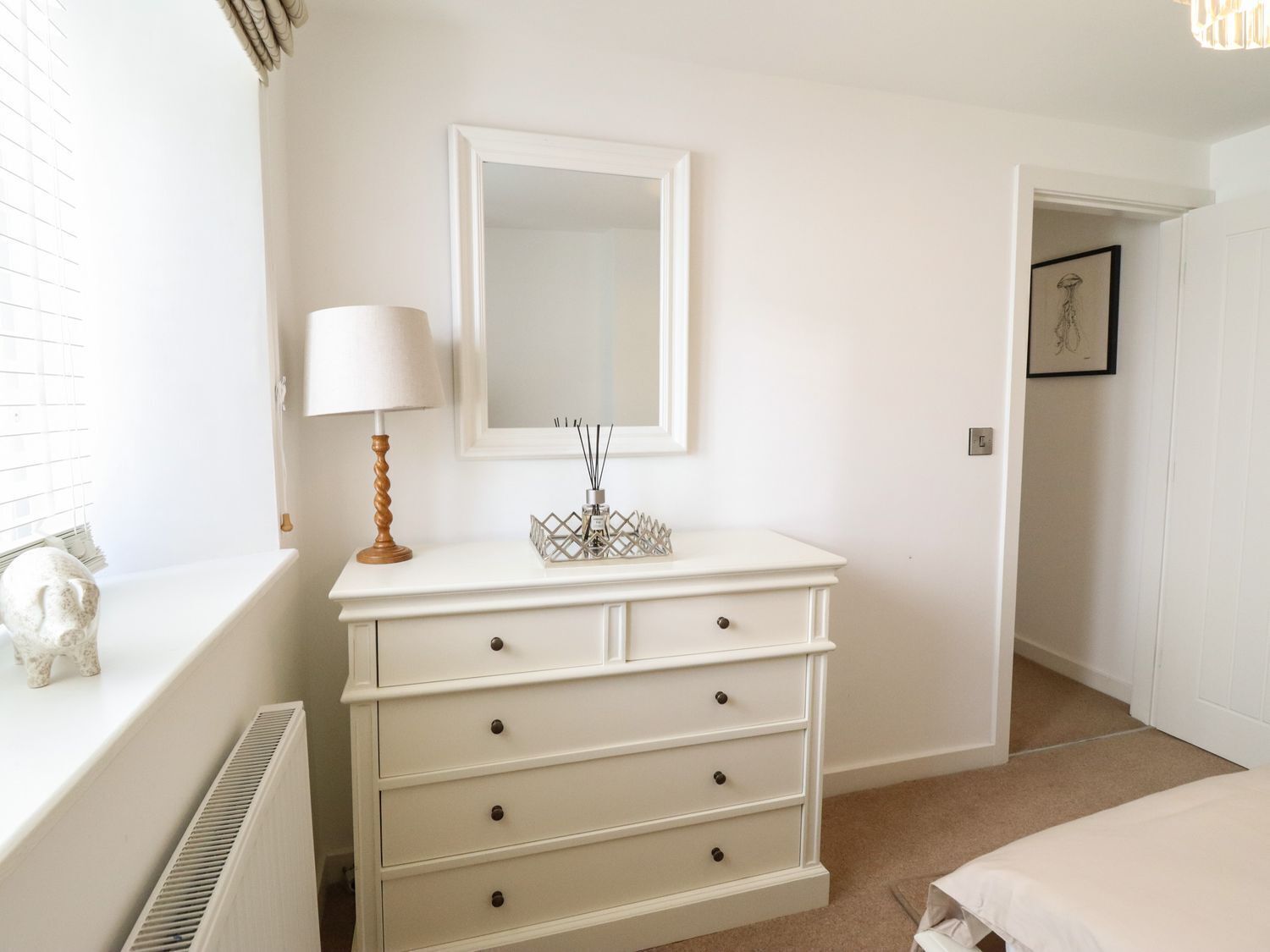 A white dresser with drawers, a mirror above it, and a lamp on the left.