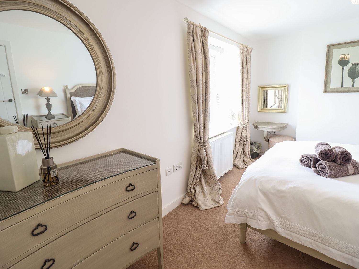Une chambre avec un grand miroir rond, une table de chevet avec une lampe, un lit avec des serviettes pliées, une petite table de chevet et une fenêtre avec des rideaux.