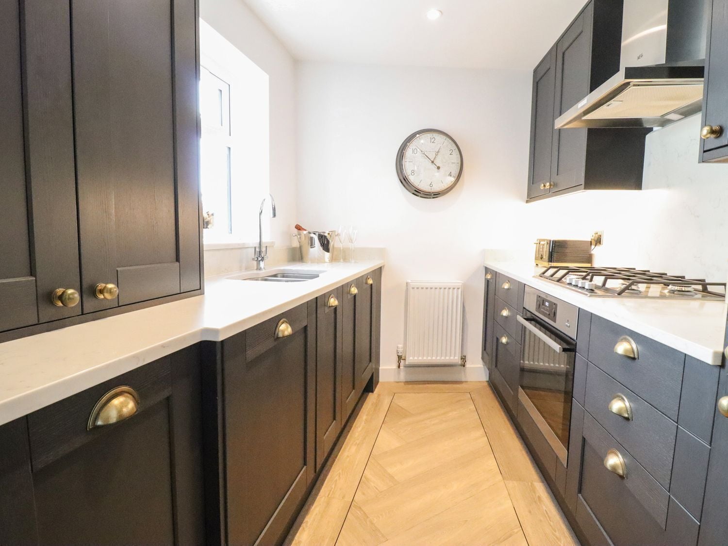 A modern kitchen with dark cabinets, a white countertop, a built-in stove, and a wall clock.