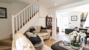 A living room with a staircase, a sofa set, a dining area, and a kitchen visible in the background. - 3 Rosemary Lane (Conwy)