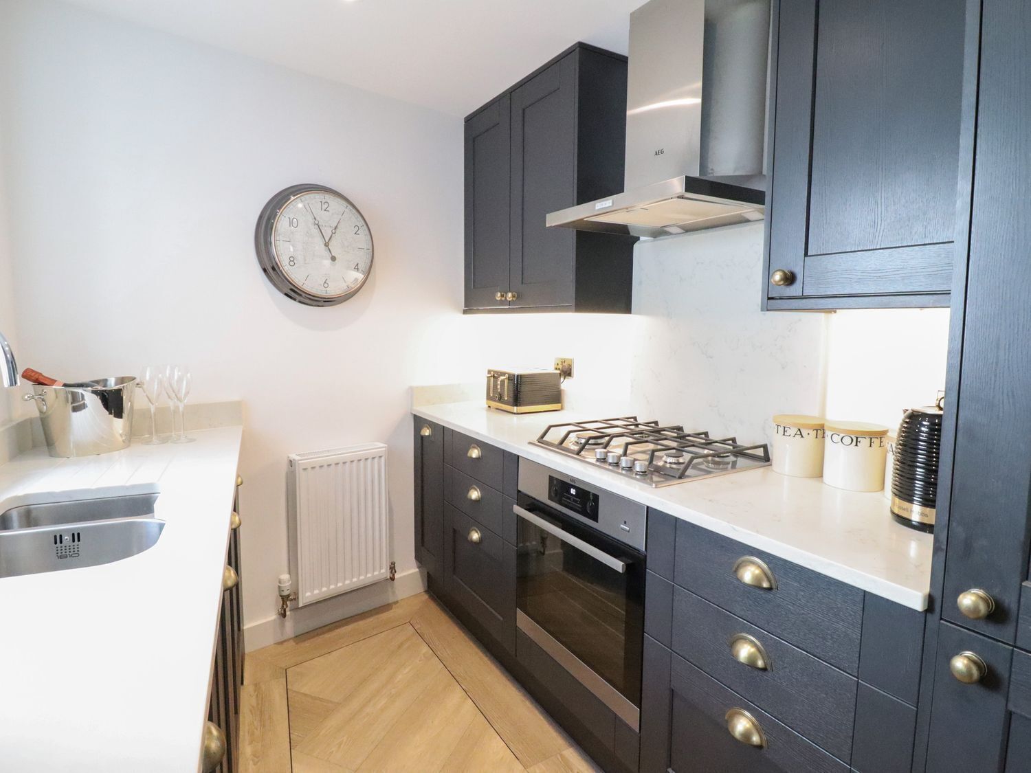 A modern kitchen with dark cabinets, a gas stove, a built-in oven, a clock, and a radiator.