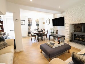 A modern living room with a fireplace, a dining area with a chandelier, and a flat-screen TV mounted on a stone wall.