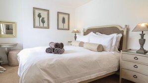 A neatly made bed with rolled towels, a bedside lamp, and a nightstand with a lamp. - 3 Rosemary Lane (Conwy)