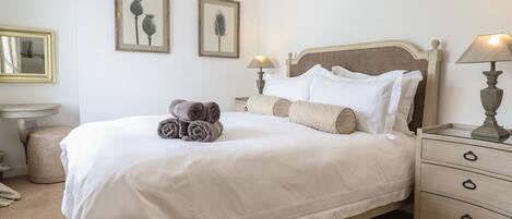 Una cama bien hecha con toallas enrolladas, una lámpara de noche y una mesita de noche con lámpara.