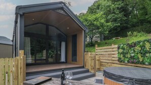 A modern outdoor seating area with a wooden table, a hot tub, and a glass-enclosed structure.