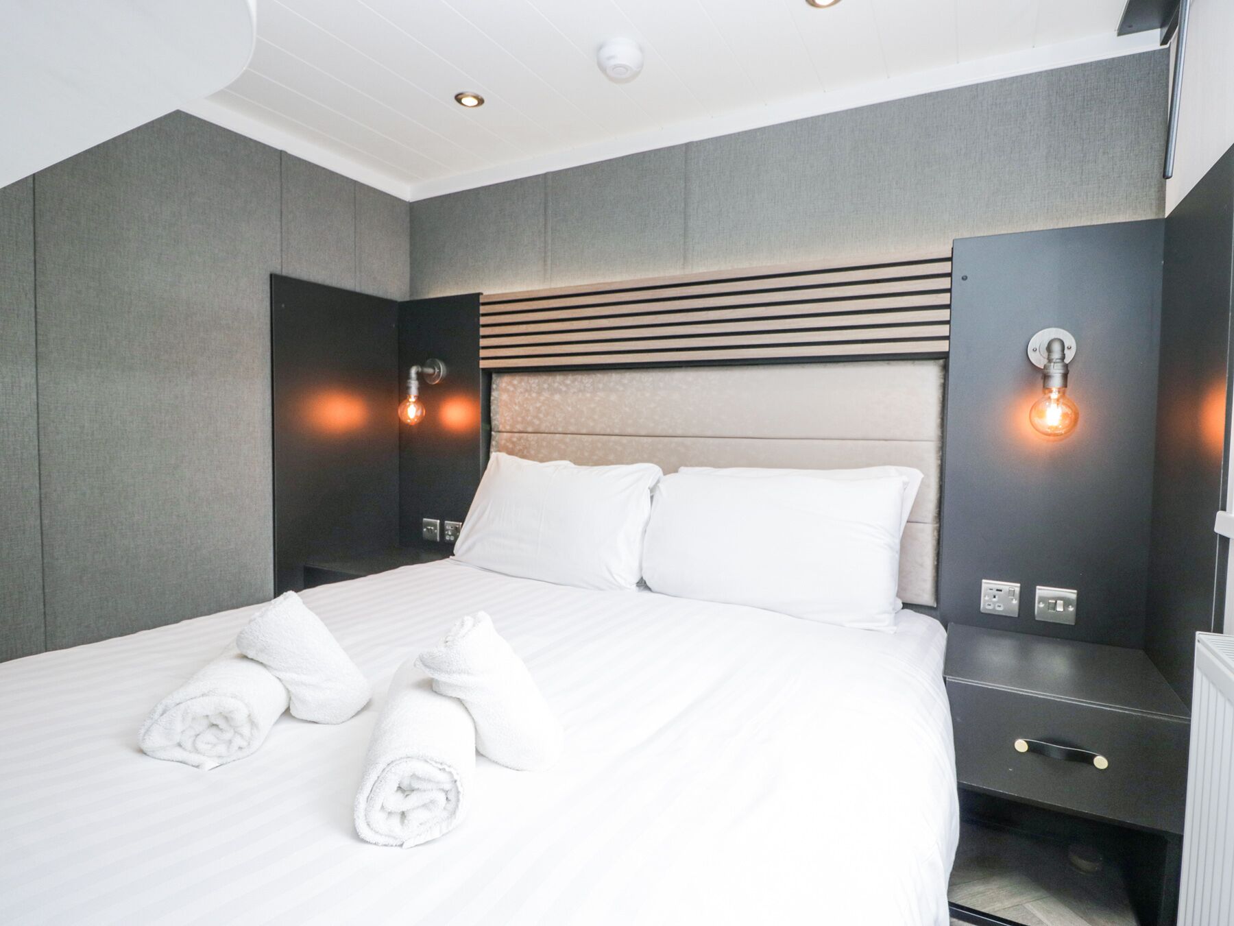 A modern hotel room with a large bed, two bedside tables, and wall-mounted light fixtures.