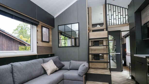 A modern living room with a grey sectional sofa, a wooden coffee table, and a staircase leading to an upper level.