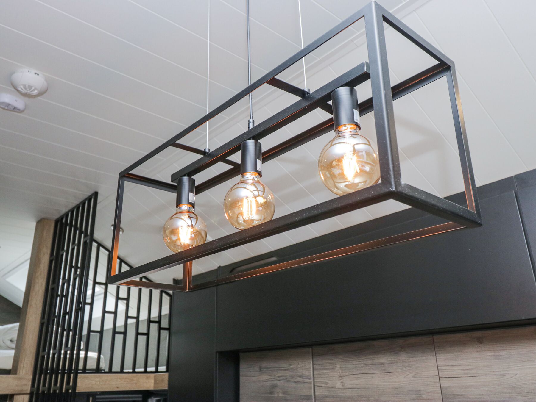Un lustre moderne composé de trois ampoules en verre suspendues à une armature métallique.