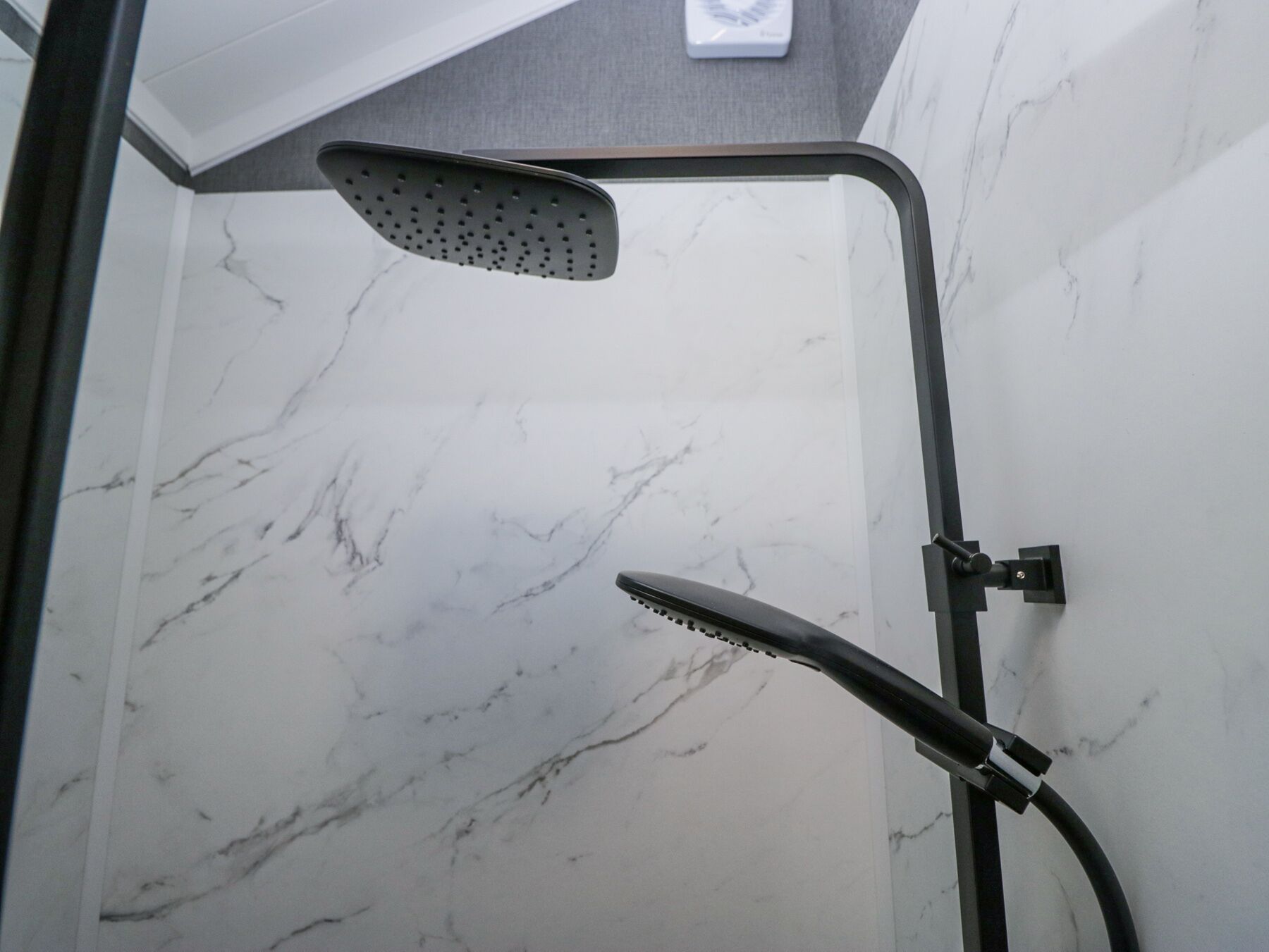 Une douche équipée d’un pommeau de douche à main et d’un pommeau de douche fixe au plafond, dans une salle de bain aux murs recouverts de marbre.