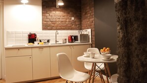 A modern kitchen with white cabinets, a brick wall, a microwave, and a dining area with white chairs and a small table. - Cracow Fancy Brick #4 - Old Town (Kraków)
