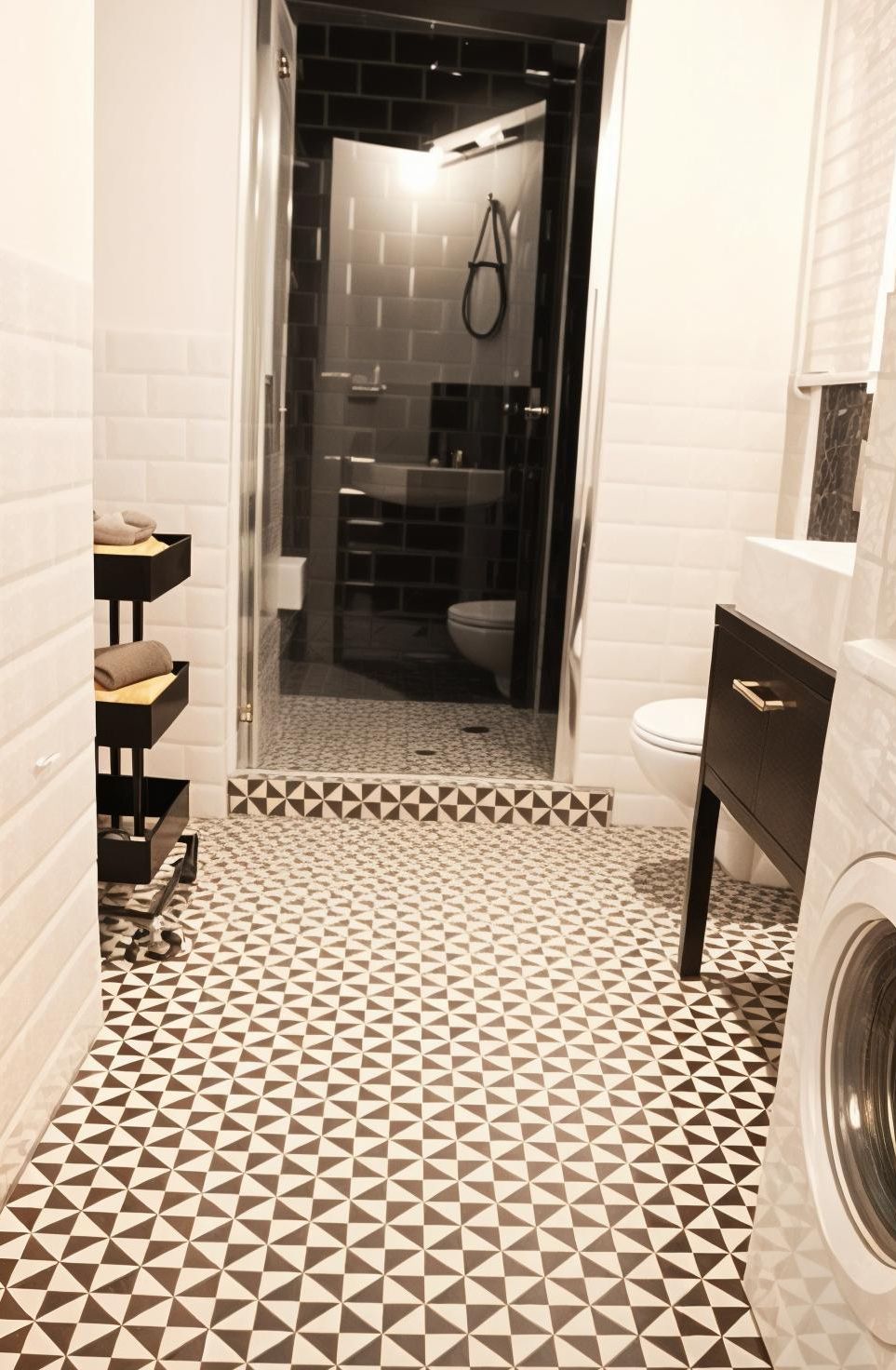 Un baño con piso de diseño geométrico, cabina de ducha de vidrio, inodoro blanco y lavamanos negro con toallero.