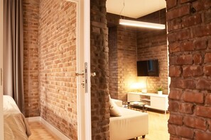 A modern room with exposed brick walls, a flat-screen TV mounted on the wall, a white sofa, and a small round table. - Cracow Fancy Brick #4 - Old Town (Kraków)