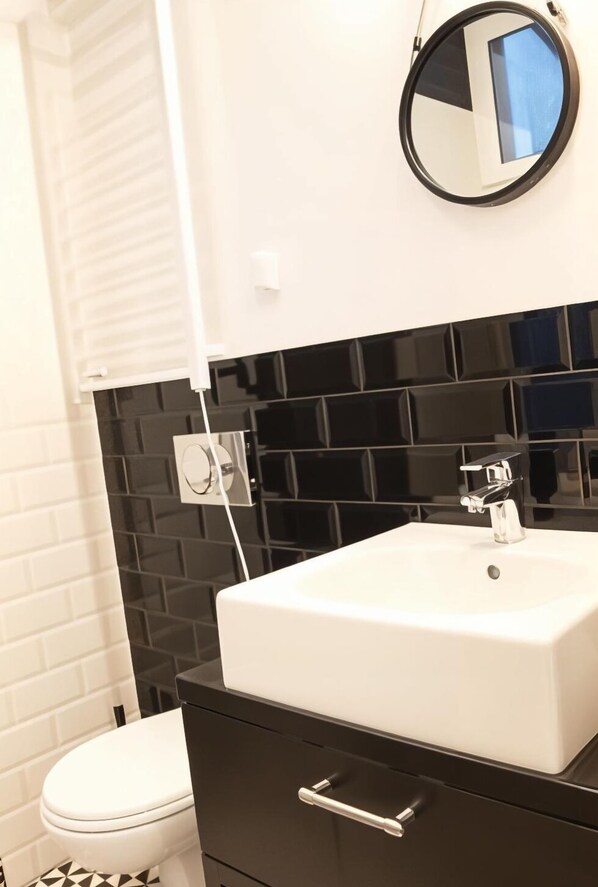 A modern bathroom with a white sink, black tiled backsplash, and a round mirror. - Cracow Fancy Brick #4 - Old Town (Kraków)
