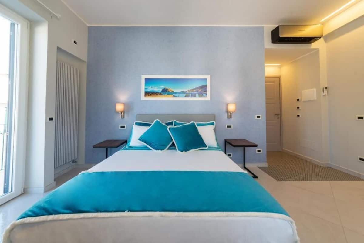 A hotel room with a large bed, a view of the sea, and a painting on the wall.