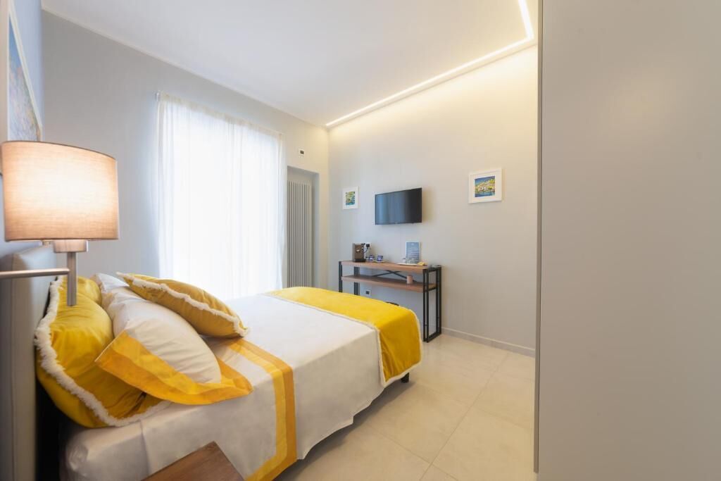 Quarto de hotel com cama, escrivaninha, televisão e janela com cortinas.