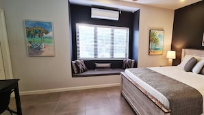 A bedroom with a large bed, a window with blinds, a built-in bench, and two wall-mounted paintings. - New spacious luxury 4-bedroom villa in gated development close to beaches. (Canaan)