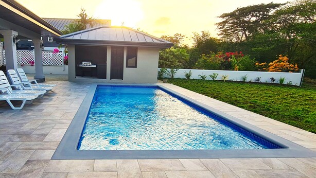 A swimming pool with lounge chairs, a covered patio, and a garden area. - New spacious luxury 4-bedroom villa in gated development close to beaches. (Canaan)