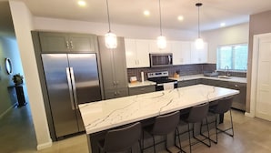 A modern kitchen with a marble island, stainless steel appliances, and pendant lighting. - New spacious luxury 4-bedroom villa in gated development close to beaches. (Canaan)