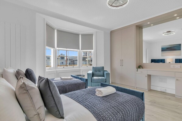 Une chambre d’hôtel avec deux lits, un coin salon, un bureau et une grande fenêtre donnant sur la ville.