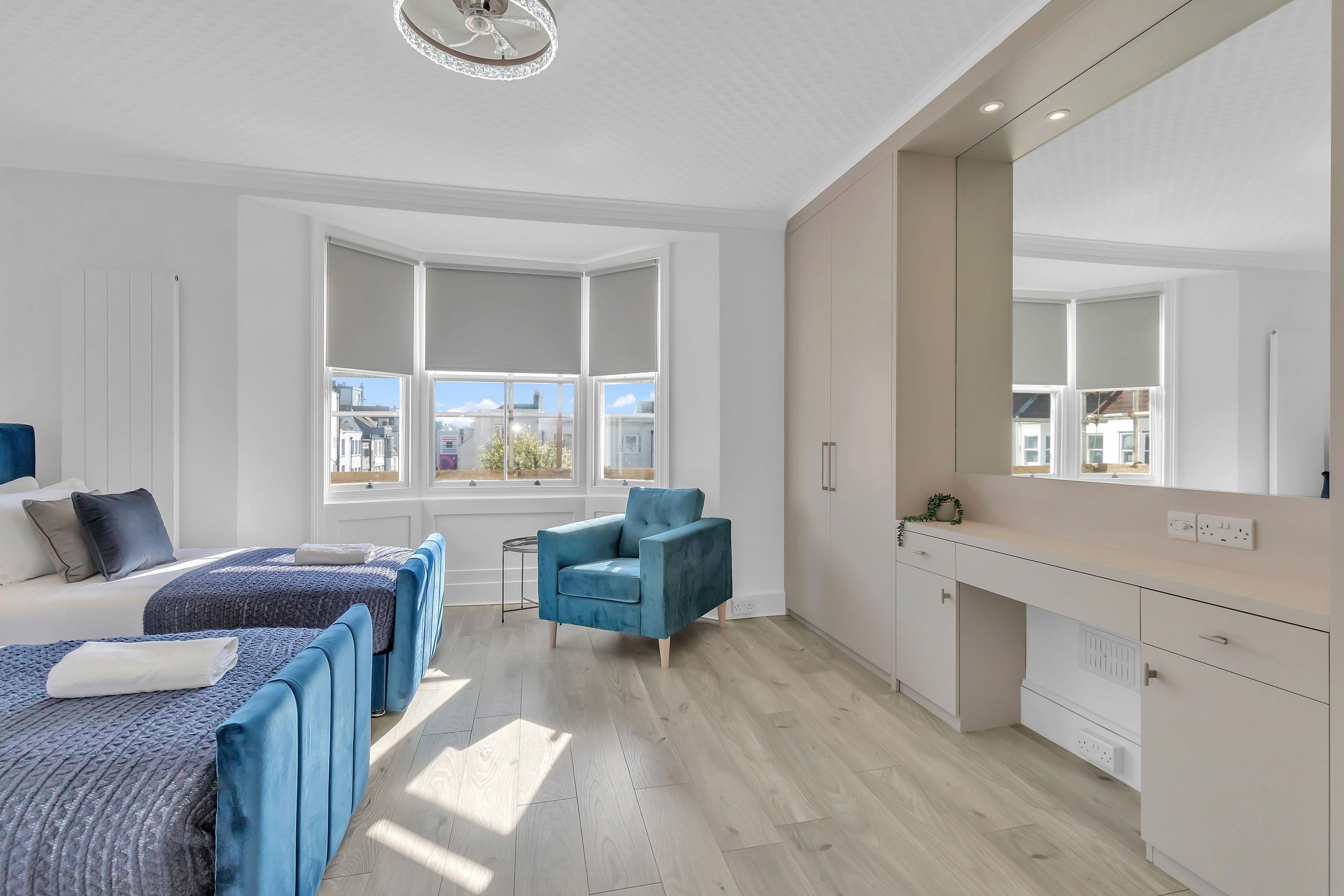 A modern bedroom with a large window, a blue armchair, and a bed with a patterned bedspread.
