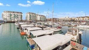 Un port de plaisance où sont amarrés de nombreux bateaux, un grand immeuble doté de balcons et un ciel d’un bleu limpide.
