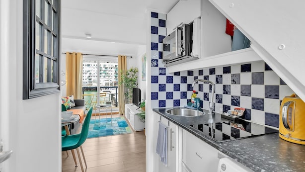 Une cuisine moderne équipée d’un four à micro-ondes, d’un évier et d’une bouilloire. Elle se distingue par son dosseret à carreaux et offre une vue sur la ville grâce à de grandes fenêtres.