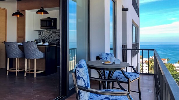 A balcony with a table and chairs, a kitchen area, and a view of the ocean.