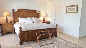 Un dormitorio con una cama de madera, dos mesitas de noche con lámparas, una puerta y un cuadro enmarcado en la pared.