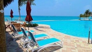 Un área junto a la piscina con sillones de descanso, piscina y vista al océano.