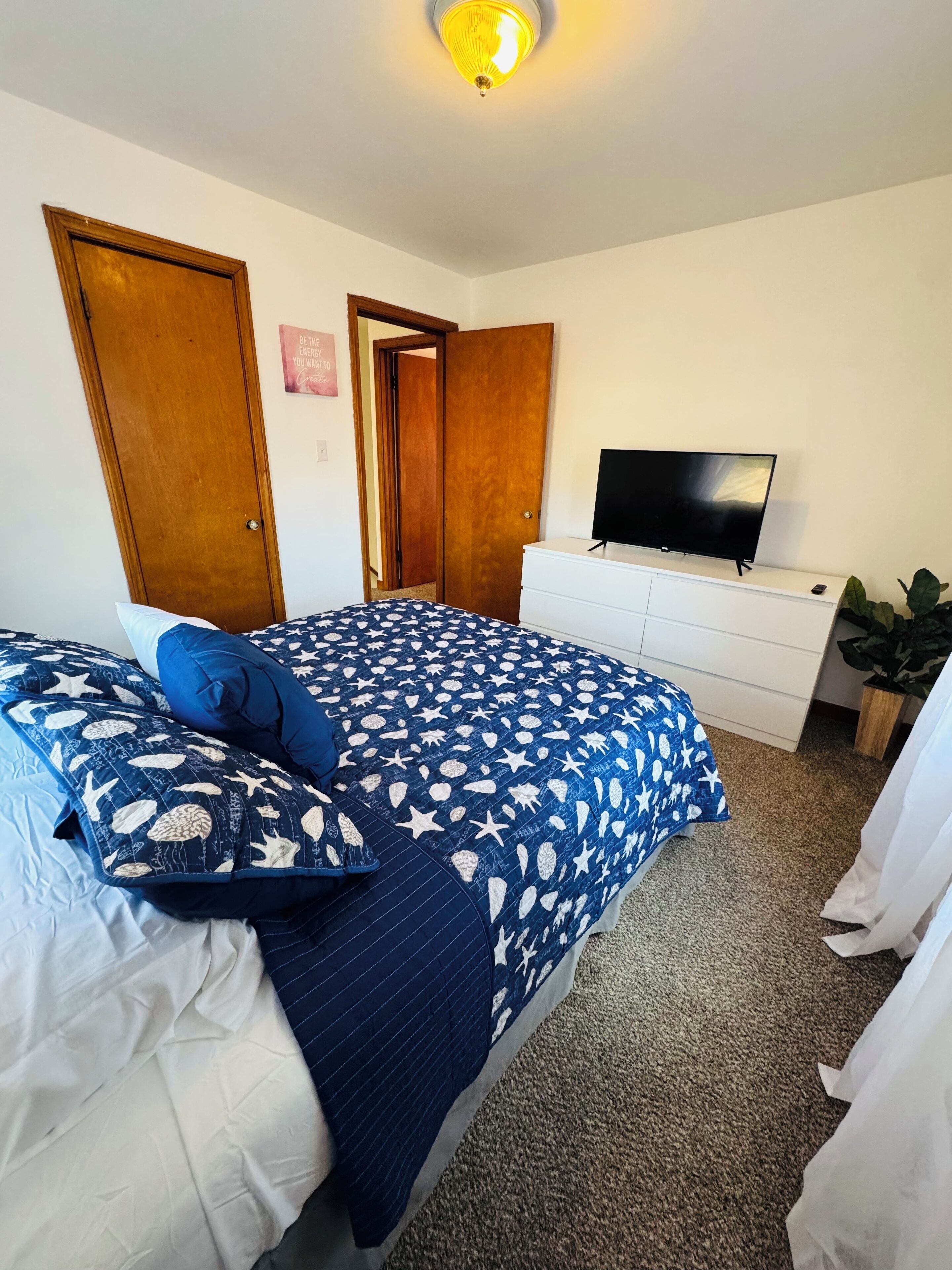 A bedroom with a bed, a dresser, a television, and a door.