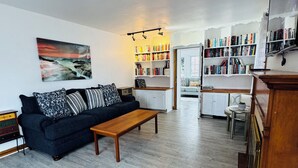 Ein Wohnzimmer mit einem dunkelblauen Sofa, einem Holztisch und einem Bücherregal voller Bücher.