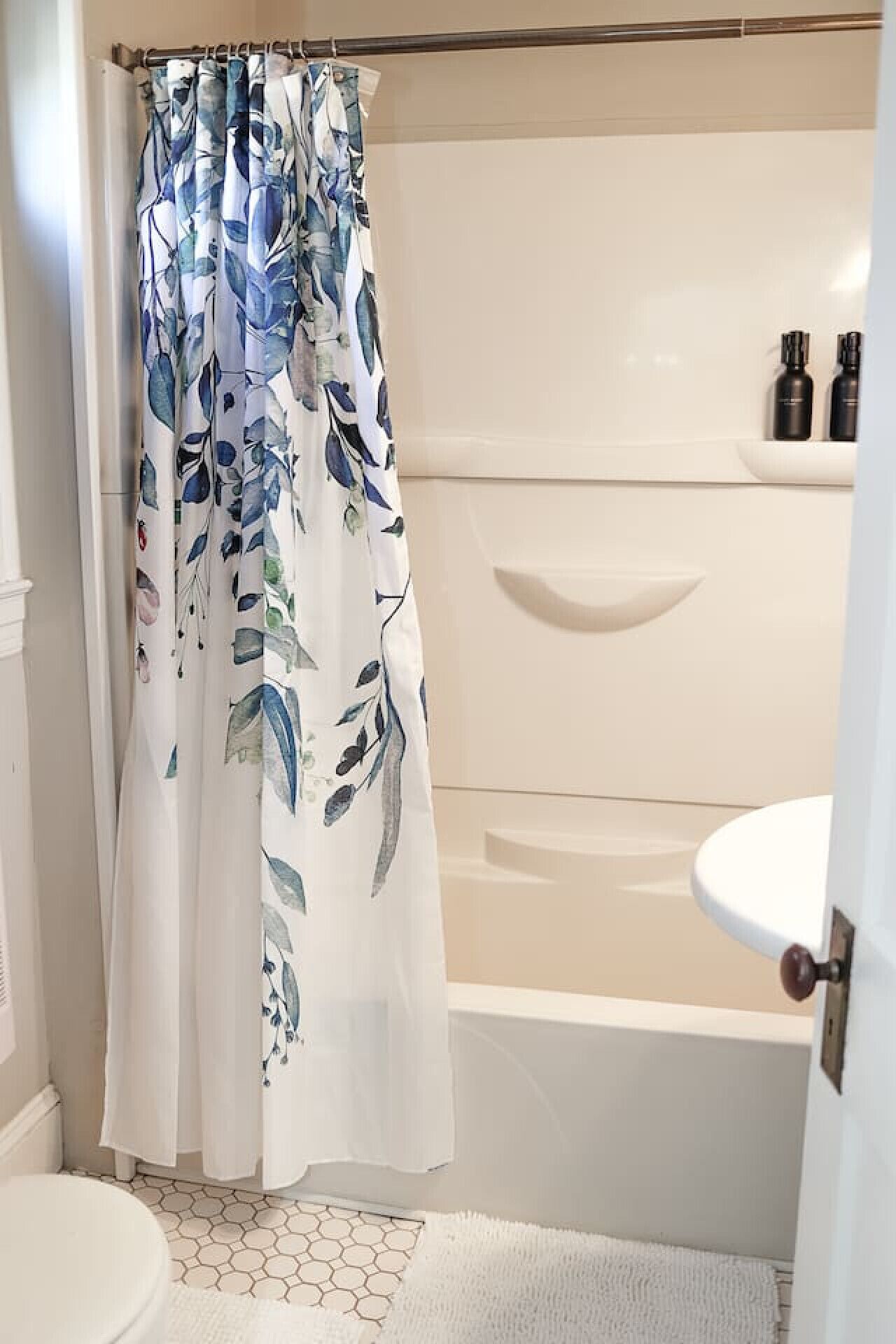 A bathroom with a shower curtain featuring a blue and white leaf pattern, a white sink, and a hexagonal patterned floor.