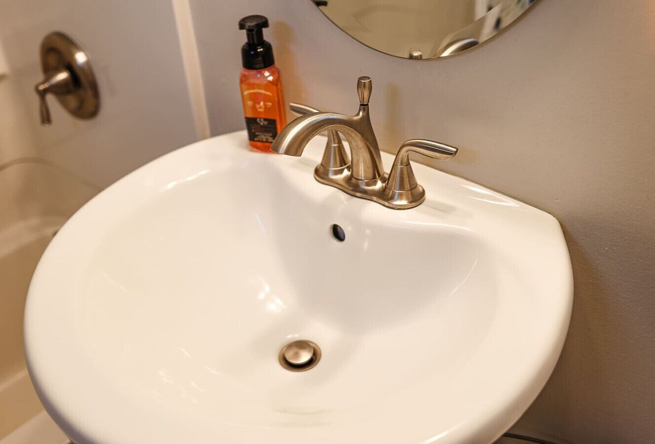 A white bathroom sink with a modern faucet and a bottle of orange soap.