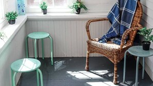A cozy corner with a wicker chair, a small stool, and a window with potted plants. - Dutch Retreat • Near Lakes • Walk Town (Bridgton)