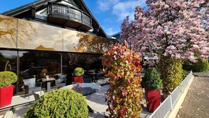An outdoor seating area with tables and chairs, surrounded by well-maintained shrubs and flowering trees. - Villa am Park (Bad Zwischenahn)