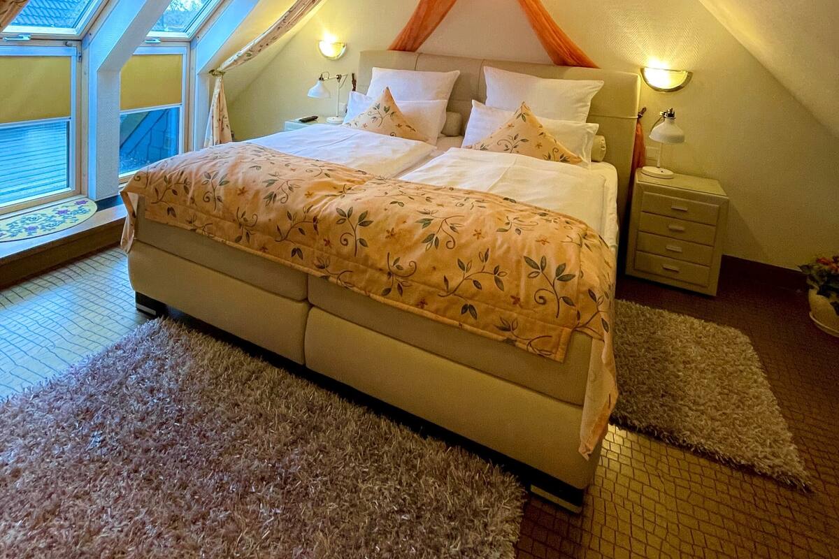 A bedroom with a large bed, a nightstand, a lamp, and a window with curtains.