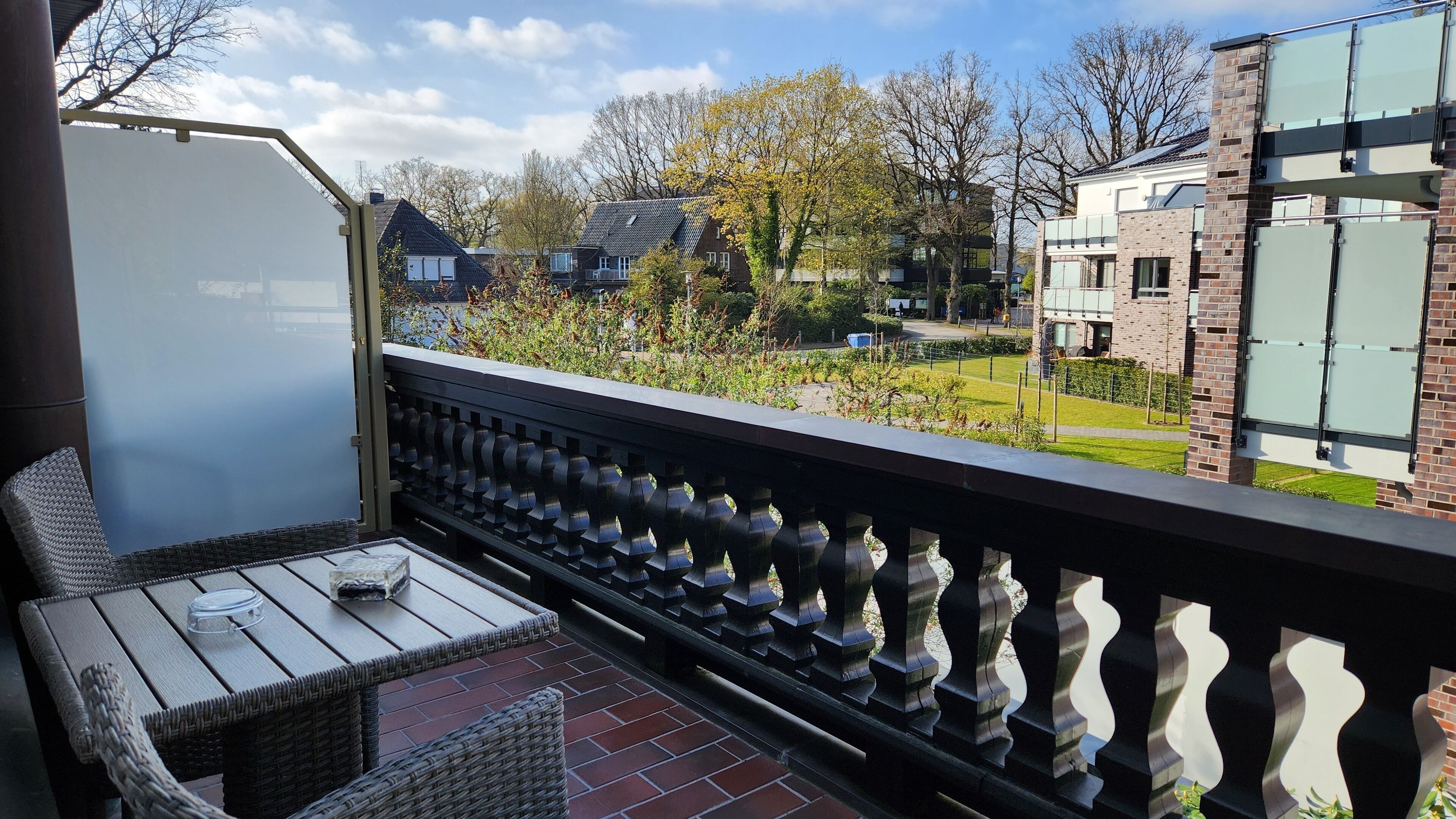 Een balkon met rieten meubilair en uitzicht op een woonwijk met huizen en bomen.