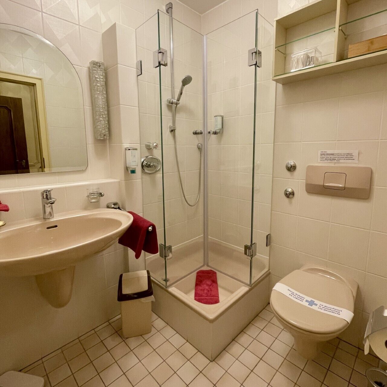 Et badeværelse med håndvask, spejl, bruser, toilet og opbevaringshylder.