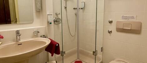 Un baño con lavamanos, espejo, ducha, inodoro y estantes de almacenamiento.