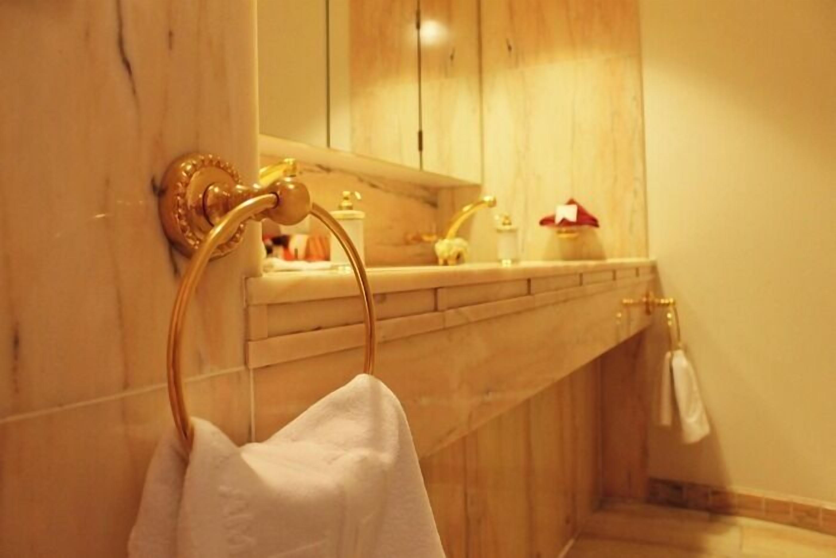 A bathroom with a marble wall, a gold towel ring, and a sink with a mirror above it.