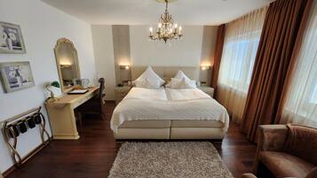 A spacious bedroom with a large bed, a desk, a chair, a mirror, and a chandelier.