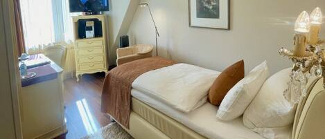 A hotel room with a bed, a desk, a television, a chandelier, and a framed picture on the wall.