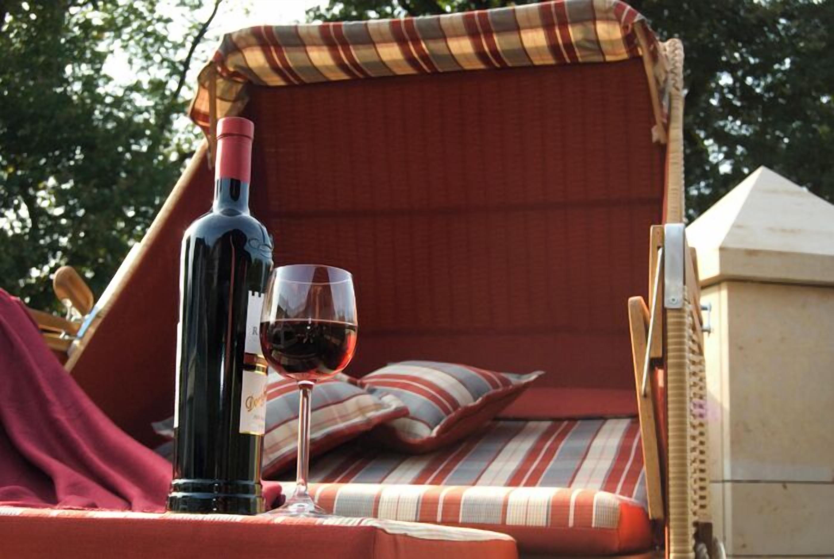 A cozy outdoor seating area with a wicker chair, a striped cushion, and a bottle of red wine on a table.