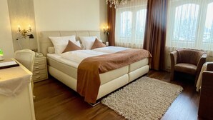 A bedroom with a large bed, a desk, a chair, a chandelier, and a view of the outdoors through the window. - Villa am Park (Bad Zwischenahn)